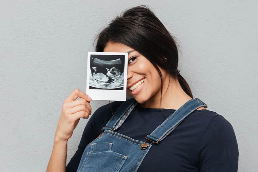 A smiling woman in overalls holding a fake ultrasound