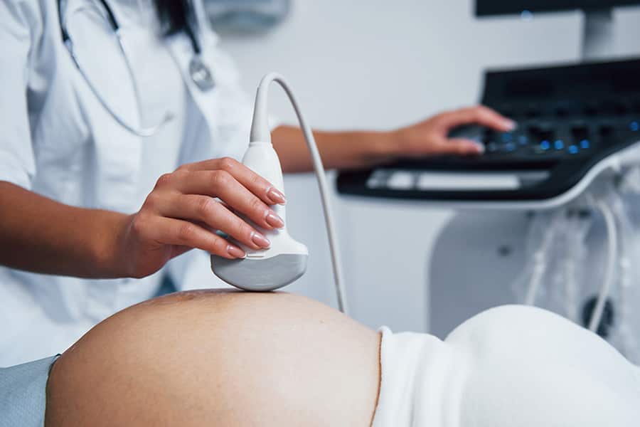 A medical professional scanning a pregnant belly with an ultrasound wand