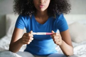 A woman holds a positive pregnancy test on a bed