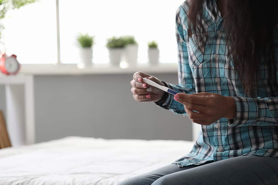 A woman on a bed looks at a pregnancy test