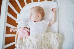A baby sleeping in a side bed crib
