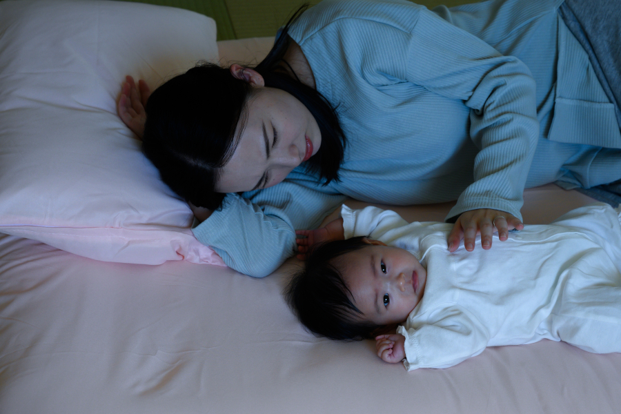 A mom sleeps next to an awake baby