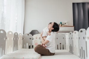 A parent hugs a baby in a playpen